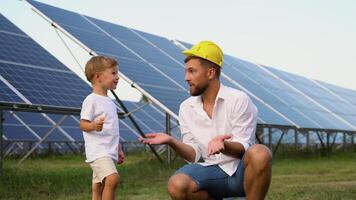 Funny father in a children's helmet and his little son near the solar panels video