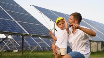un padre y su pequeño hijo en un amarillo casco cerca el solar paneles video