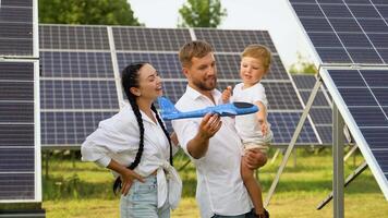 familia con solar panel granja, verde energía concepto. amoroso familia participación su niño en frente de solar panel en un soleado día y jugando con juguete aviones video