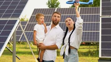 família com solar painéis, renovável energia conceito. pais e bebê filho jogando juntos com brinquedo aviões perto solar painéis video