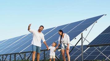 Happy family of three enjoying a stroll in a sunny day near a large solar panel farm video