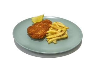 Breaded steak with French fries, two lemon wedges, served on a turquoise plate. Isolated in a white background. photo