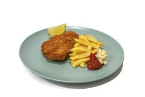 Breaded steak with French fries, with ketchup and mayonnaise, two lemon wedges, served on a turquoise plate. Isolated in a white background. photo