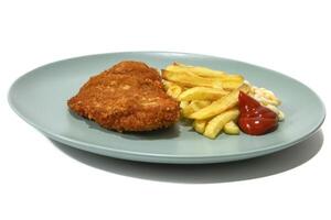 Breaded steak with French fries, topped with ketchup and mayonnaise, served on a turquoise plate. Isolated on a white background. photo