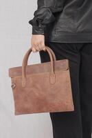 A woman in a black leather jacket and black pants with brown leather hand bag photo