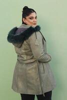 a woman in a fur hat with long green coat and black pants photo