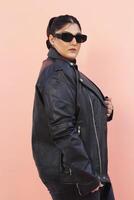 a woman in a black leather jacket and jeans posing for picture with glasses photo