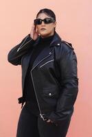 a woman in a black leather jacket and jeans posing for picture with glasses photo