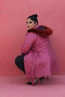 a woman in a pink long coat with fur and black pants photo