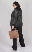 A woman in a black leather jacket and black pants with brown leather hand bag photo