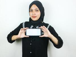 joven musulmán mujer en hijab sonriente demostración móvil teléfono blanco pantalla recomendando aplicación foto
