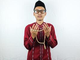 Religious asian muslim man in traditional dress using prayer beads isolated on white background photo