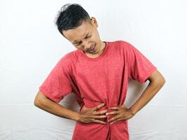 Asian man holding his stomach, feeling stomach pain, nausea, and other stomach disease concept. photo