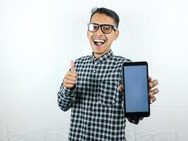 Portrait of asian man holding blank screen hand phone while giving thumbs up with smiling expression photo