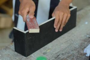 Hands of a carpenter manually sanding wooden with sandpaper in a woodworking or carpentry workshop photo