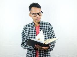 Handsome Asian student smiling and holding and reading book in hand photo