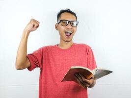 retrato de sonriente asiático hombre participación y leyendo libro mientras apretando puño. foto