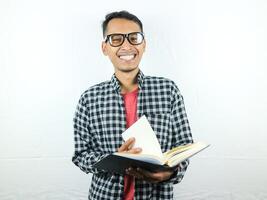 Handsome Asian student smiling and holding and reading book in hand photo