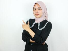 Beautiful Asian Muslim woman in hijab, smiling pointing fingers a side at copy space. photo