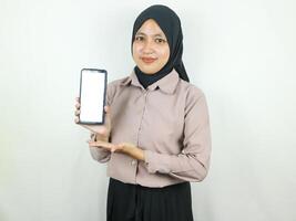Young Muslim woman in hijab smiling showing mobile phone blank screen recommending App photo
