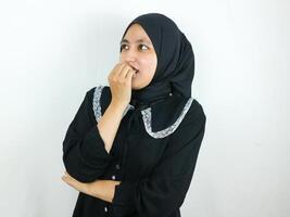 Smiling asian muslim woman biting finger and looking aside thinking or having interesting idea photo