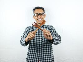 emocionado asiático hombre participación cuchara y tenedor en su manos foto