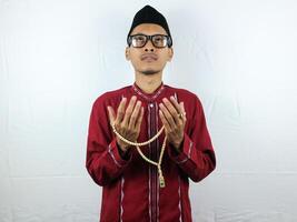 Religious asian muslim man in traditional dress using prayer beads isolated on white background photo