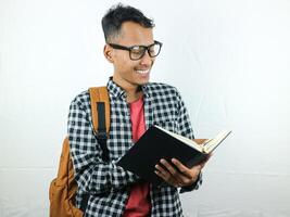 Handsome Asian student smiling and holding and reading book in hand photo