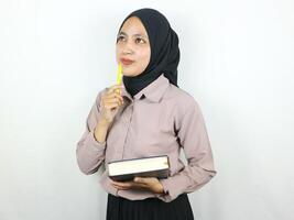 retrato hermosa asiático mujer en hijab participación libro y bolígrafo, pensando acerca de algo. foto