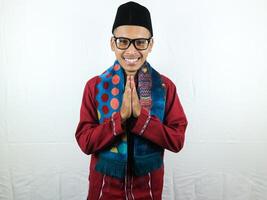 Asian Muslim man wearing glasses smiling to give greeting during Ramadan and Eid Al Fitr celebration over white background photo