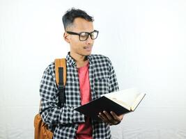 Handsome Asian student smiling and holding and reading book in hand photo