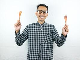 Excited Asian man holding spoon and fork in his hands photo