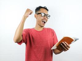 portrait of smiling asian man holding and reading book while clenching fist. photo