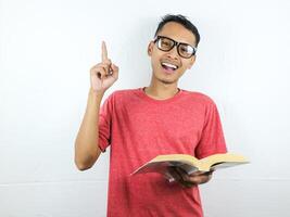 portrait of smiling asian man holding book and pointing finger up getting idea. photo