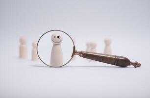 Magnifying glass focus wood doll which is among crowd for human development recruitment leadership and customer target group HRM or Human Resource Management concept photo