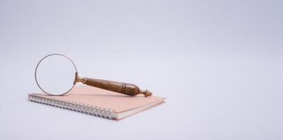 magnifying glass and spiral notebook on white table background photo