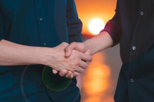 two men doing a handshake with blurred sunset background in concept of friendship partner and business dealing photo