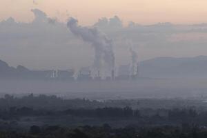 A factory emits smoke from its stacks, and Air pollution over the coal power plant Mae Moh Lampang in the morning with fog, Suitable for industrial and environmental themes photo