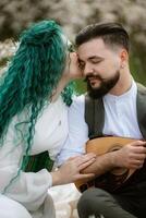 a bearded groom plays a stringed instrument and a girl with sits in a spring meadow photo