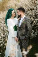 a bearded groom plays and a girl with green hair against the background of blooming spring photo