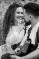 a bearded groom plays a stringed instrument and a girl sits in a spring meadow photo