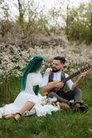 a bearded groom plays a stringed instrument and a girl sits in a spring meadow photo