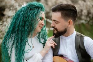 a bearded groom plays a stringed instrument and a girl with sits in a spring meadow photo