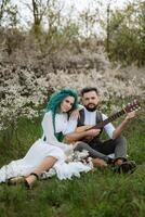 a bearded groom plays a stringed instrument and a girl sits in a spring meadow photo