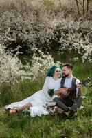 a bearded groom plays a stringed instrument and a girl sits in a spring meadow photo