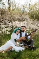 a bearded groom plays a stringed instrument and a girl sits in a spring meadow photo