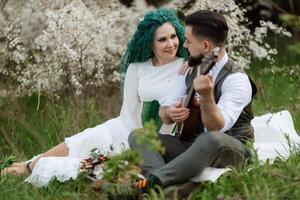 a bearded groom plays a stringed instrument and a girl sits in a spring meadow photo