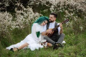 a bearded groom plays a stringed instrument and a girl sits in a spring meadow photo