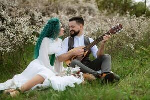 a bearded groom plays a stringed instrument and a girl sits in a spring meadow photo