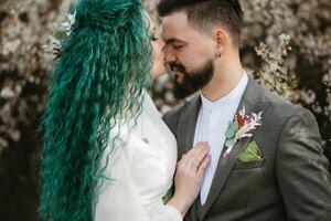 a bearded groom plays and a girl with green hair against the background of blooming spring photo